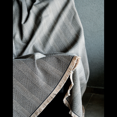 Manta xadrez cinza e bege com franjas sobre cadeira de madeira num ambiente interior