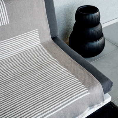 Manta cinzenta e branca com riscas sobre sofá cinzento escuro ao lado de vaso preto em chão de azulejos