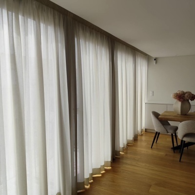 Cortinas brancas translúcidas junto a mesa de jantar com cadeiras cinza