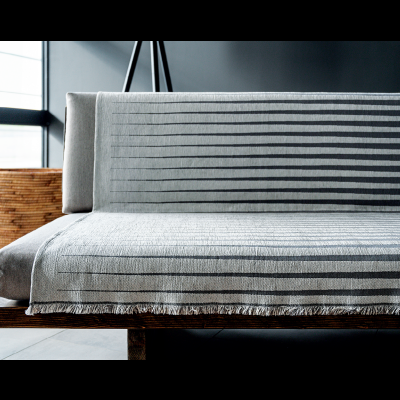 sofá de madeira com capa cinza riscada e vaso em cesto ao lado