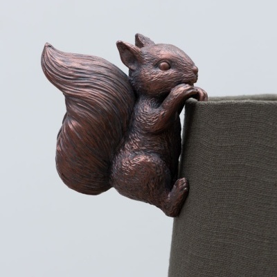 Escultura de esquilo em bronze agarrada a um vaso de tecido cinza