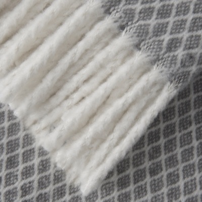 manta cinzenta com padrão de losangos e franjas brancas