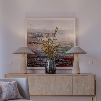 Aparador de madeira clara com lâmpadas e vaso sobre ele, pintura abstrata na parede branca