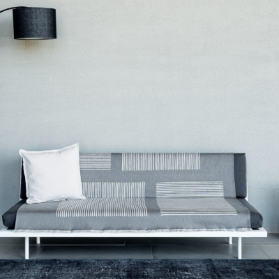 Sofá-cama cinza com padrão riscas, almofada branca, candeeiro de pé preto, tapete cinza escuro, parede cinza lisa