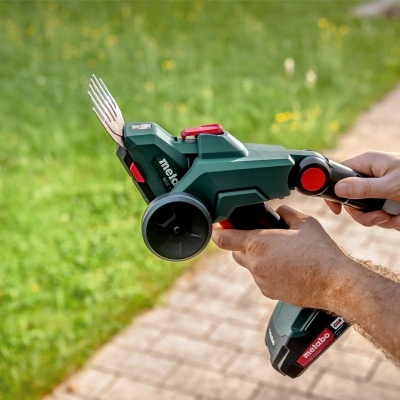 Cortador de relva manual com lâminas metálicas e pega preta com detalhes vermelhos.