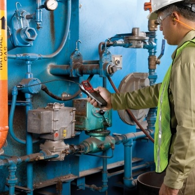Homem operando dispositivo em tubulação industrial azul e laranja