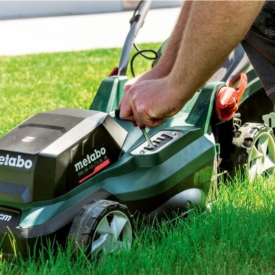 Corta-relva elétrico Metabo verde e preto com botão vermelho em relva verde