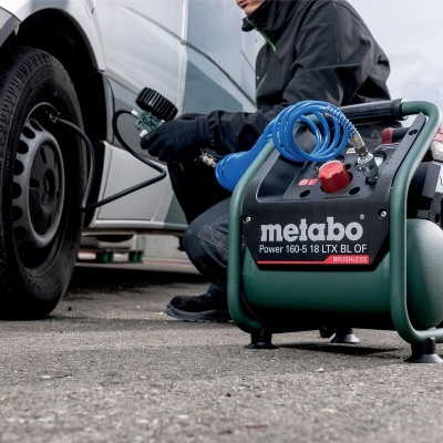 Compressor de ar Metabo com estrutura metálica cinza e corpo verde, usado para encher pneu de carro branco
