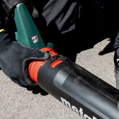 Soprador de folhas preto, verde e vermelho com luvas pretas em chão cinzento