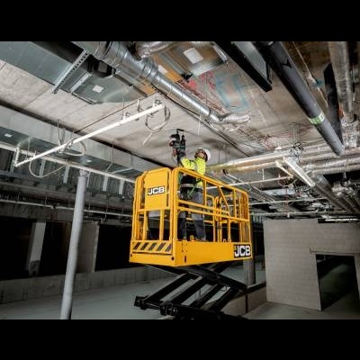 Plataforma elevatória amarela JCB em construção com tubulações e trabalhadores com coletes.