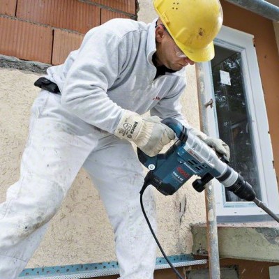 Trabalhador com capacete e pistola elétrica a perfurar parede em obra