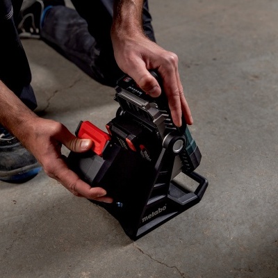 Lanterna portátil Metabo preta com vermelho em suporte negro no chão de cimento