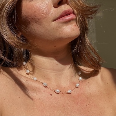 Colar feminino de pérolas irregulares brancas com detalhes dourados no pescoço de mulher.