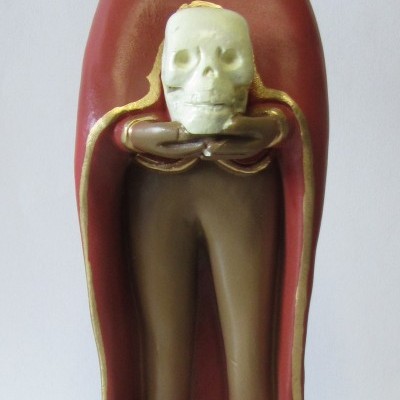 Figura esculpida de homem com capa vermelha e segurando uma caveira branca