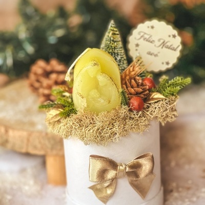Arranjo decorativo natalício com vela, pinha, musgo e laço dourado numa base branca