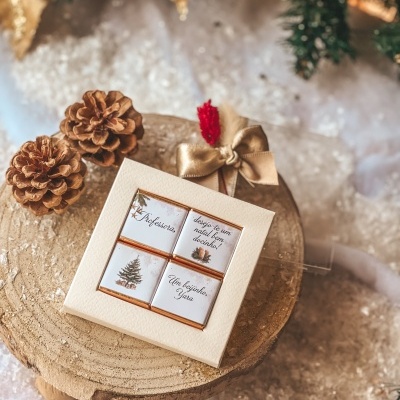 Chocolates natalícios em embalagem branca sobre suporte de madeira com decoração de pinhas e neve.