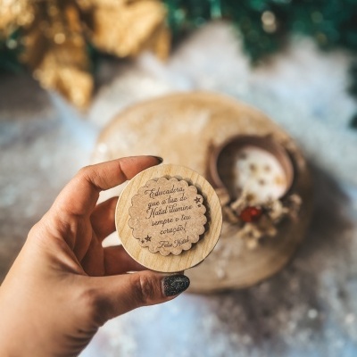 Tampa de madeira clara com mensagem de Natal, mão a segurar.