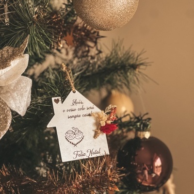 Pendentes natalícios em árvore, incluindo casa branca com mensagem para avós.