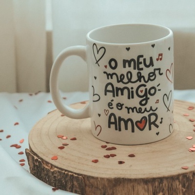 Caneca branca com texto decorativo e corações em sobre base de madeira.