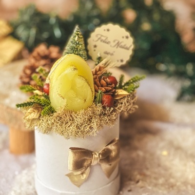 Arranjo decorativo de Natal com vela amarela e elementos naturais numa caixa branca com laço dourado