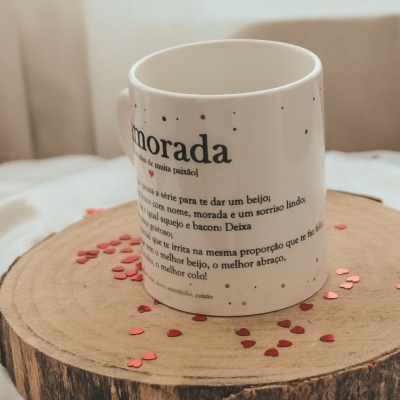 Caneca branca com texto em português sobre base de madeira e corações vermelhos ao redor