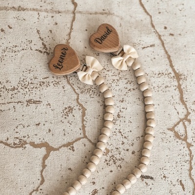Fitas de contas de madeira com corações gravados e laços sobre superfície bege fissurada
