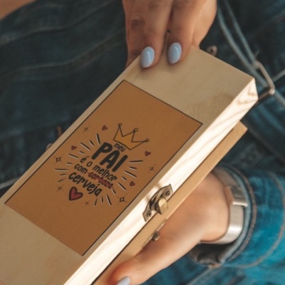 Caixa de madeira com frase para pai e detalhes decorativos, segurada por mãos com unhas azul claro
