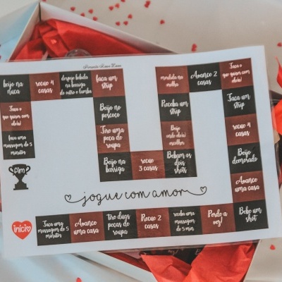 Tabuleiro de jogo com texto em português dentro de caixa branca com laço vermelho em fundo branco com corações vermelhos.