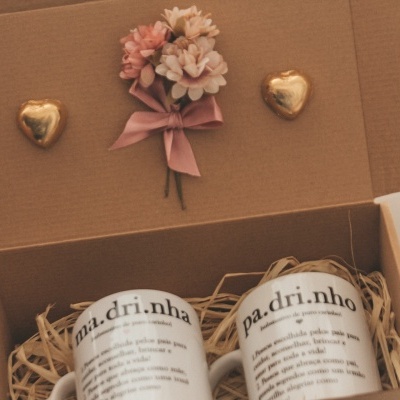 Caixa aberta com velas brancas rotuladas, flores artificiais e chocolates em forma de coração