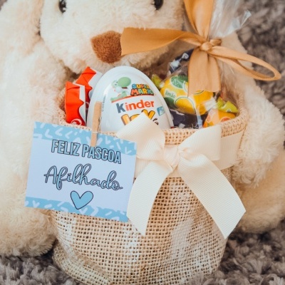Cesta de juta com chocolates Kinder e cartão de Páscoa sobre tapete cinzento
