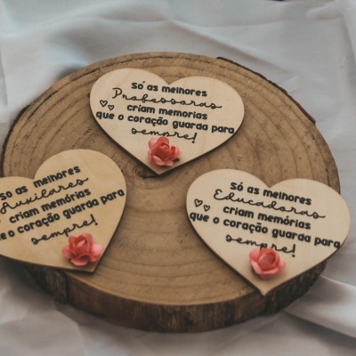 Três placas de madeira em forma de coração com texto e flores cor-de-rosa sobre madeira e tecido branco