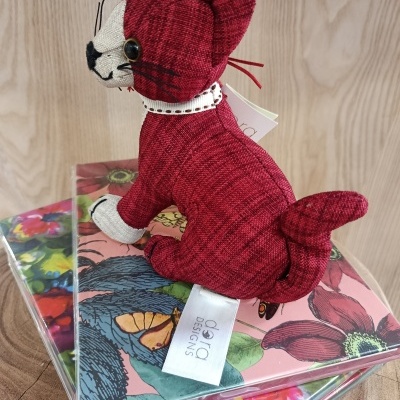 Brinquedo de gato de tecido vermelho em cima de caixas coloridas com flores.