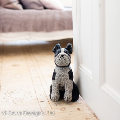 Boneco de cão cinza e preto em tecido felpudo no chão junto a porta e tapete beige