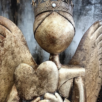 Escultura metálica de anjo dourado segurando coração com coroa flores e pedras
