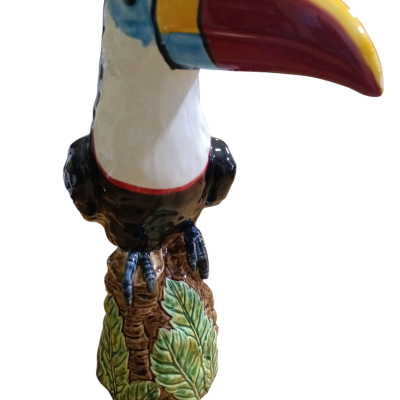 Figura decorativa de tucano colorido em cerâmica com base de folhas verdes.
