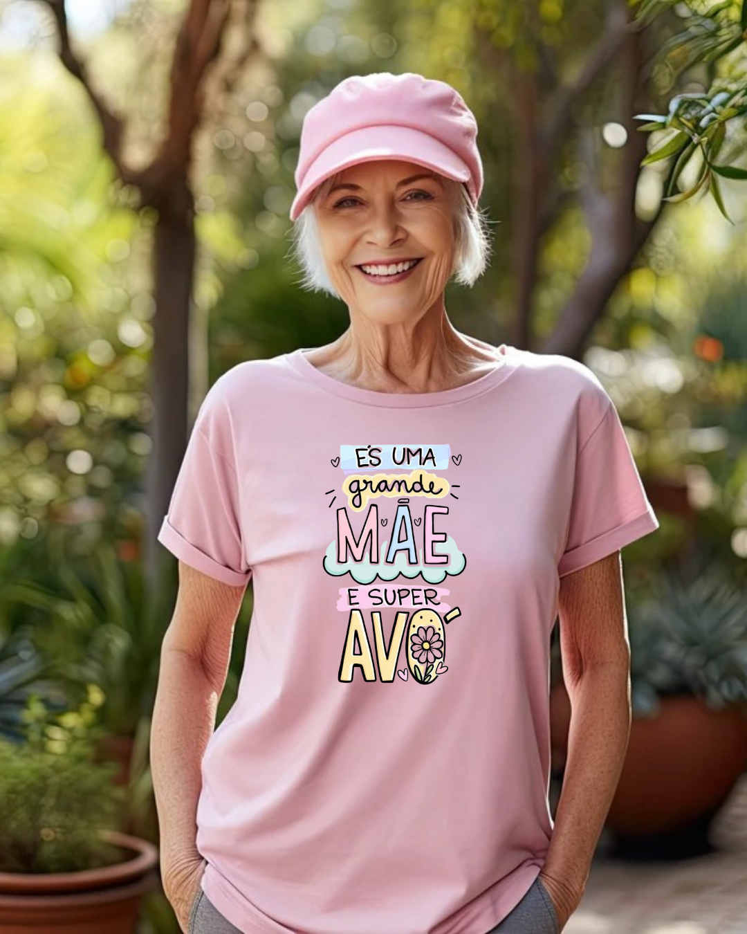 Mulher idosa com boné e t-shirt rosa com texto colorido, em ambiente exterior com plantas.