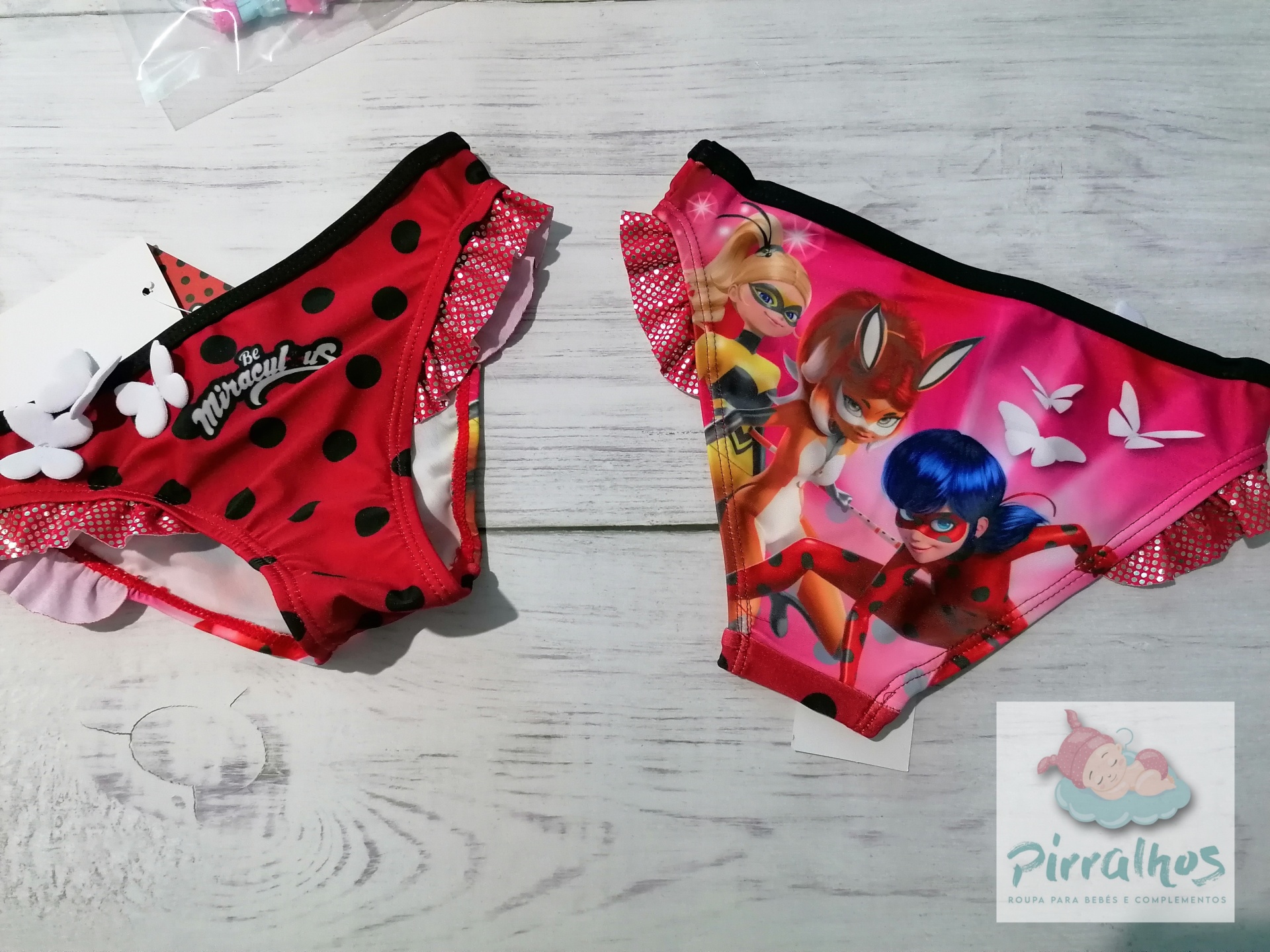 Duas cuecas de banho infantis vermelha e rosa com padrões e personagens, sobre madeira clara