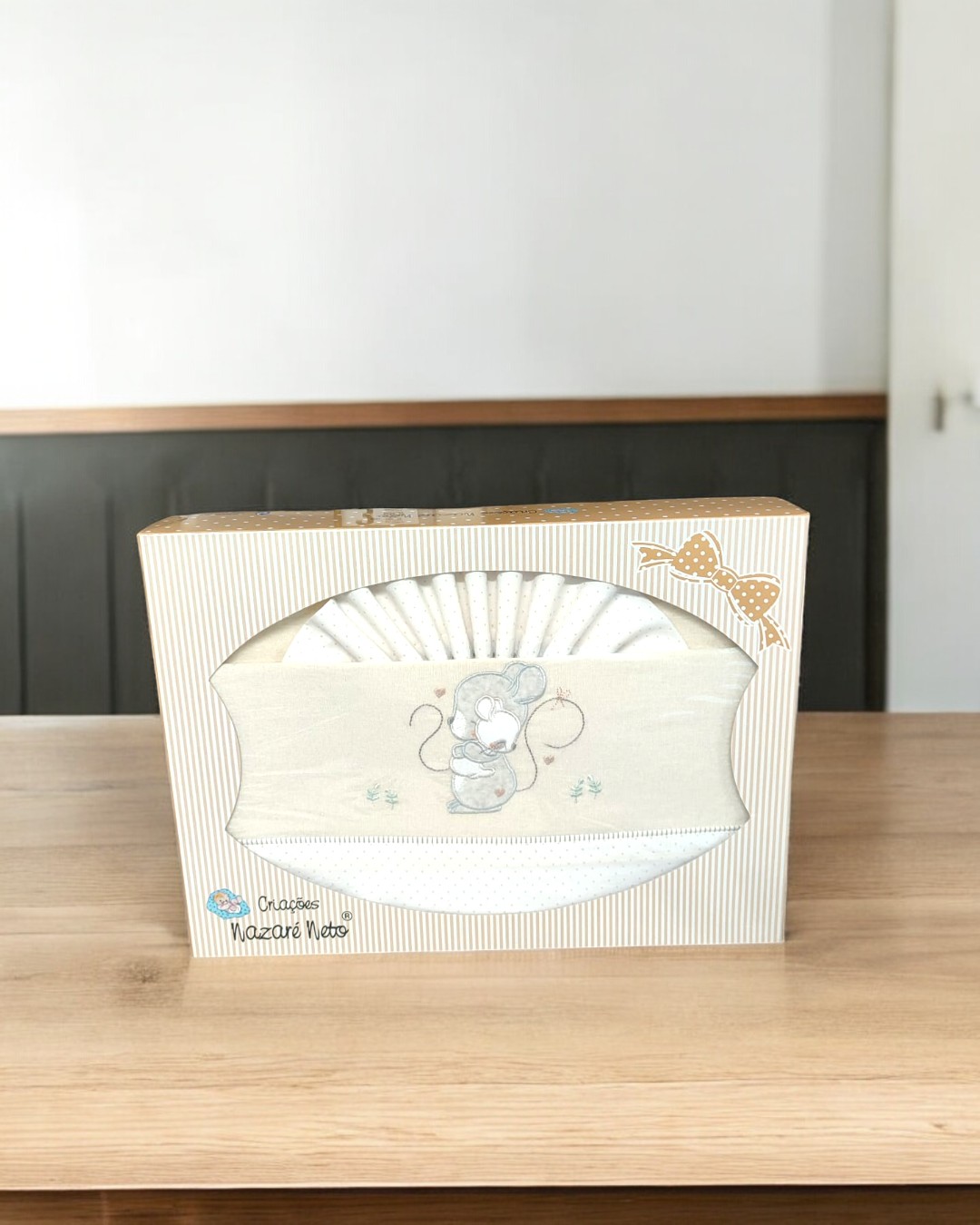 Conjunto de fraldas de bebé brancas bordadas com rato e embalagem em cartão às riscas sobre mesa de madeira
