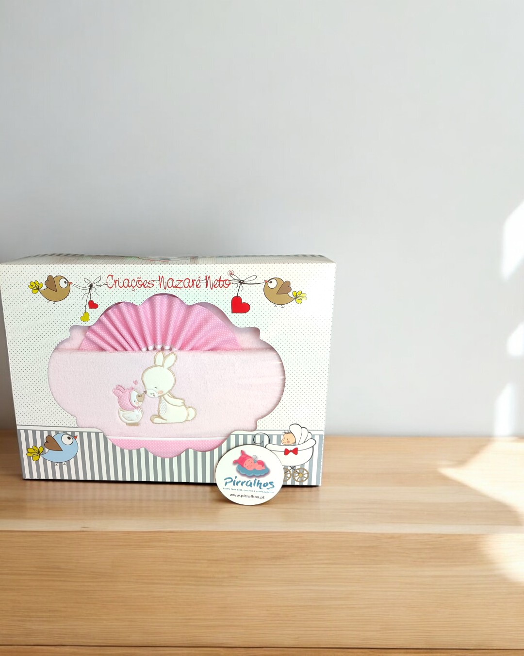 Conjunto de roupa de bebé rosa numa caixa decorativa com desenhos de pássaros e texto