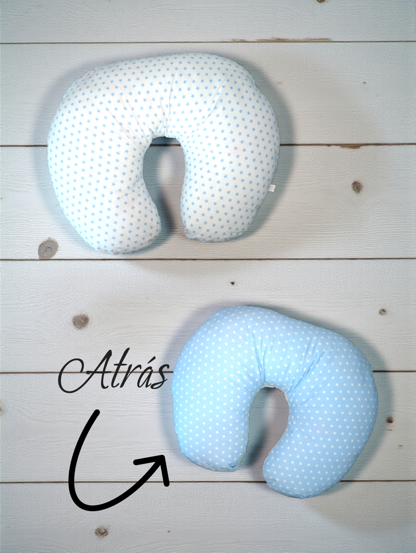 Dois almofadas U para pescoço, branco com estrelas azuis e azul com estrelas brancas, em fundo de madeira clara com texto Atrás e seta.