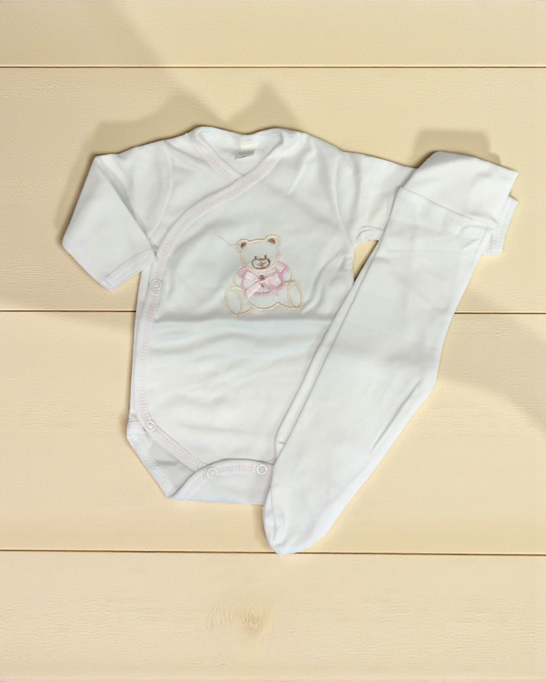 Conjunto de roupa de bebé branca com body e calças sobre superfície de madeira