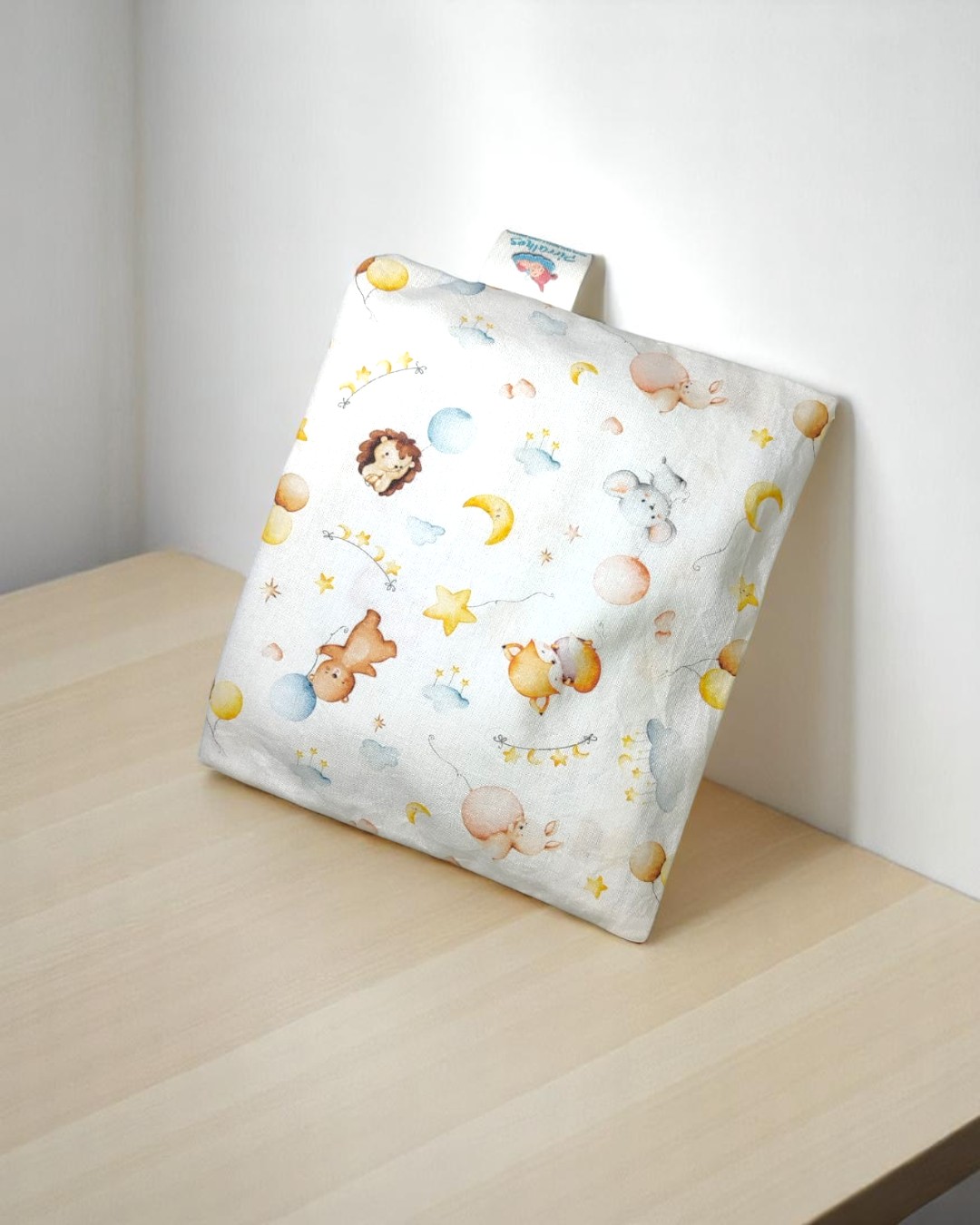 Almofada quadrada com padrão infantil colorido em ambiente minimalista.