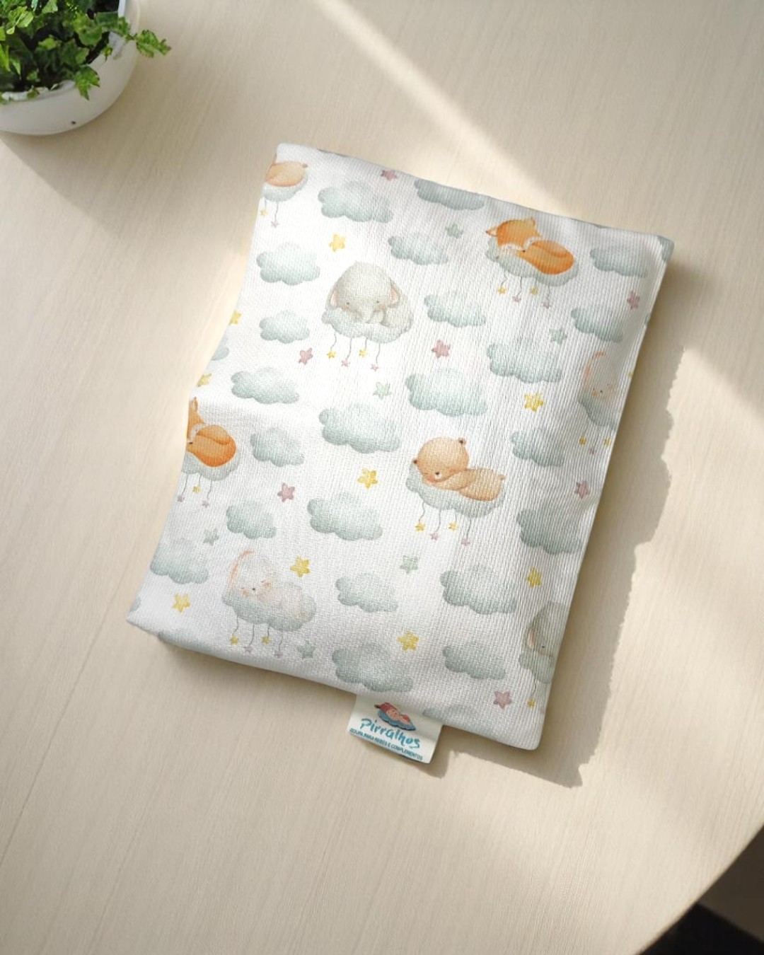 Capa de tecido com padrão de pássaros, nuvens e estrelas sobre superfície de madeira clara