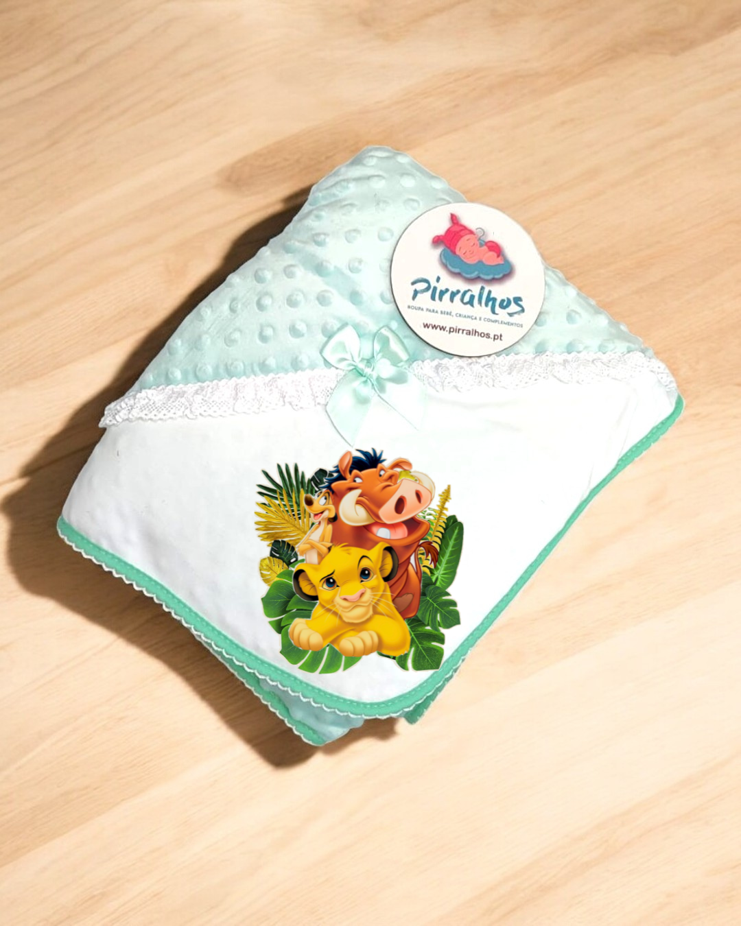 Manta de bebé azul claro com personagens do Rei Leão e etiqueta Pirralhos sobre superfície de madeira