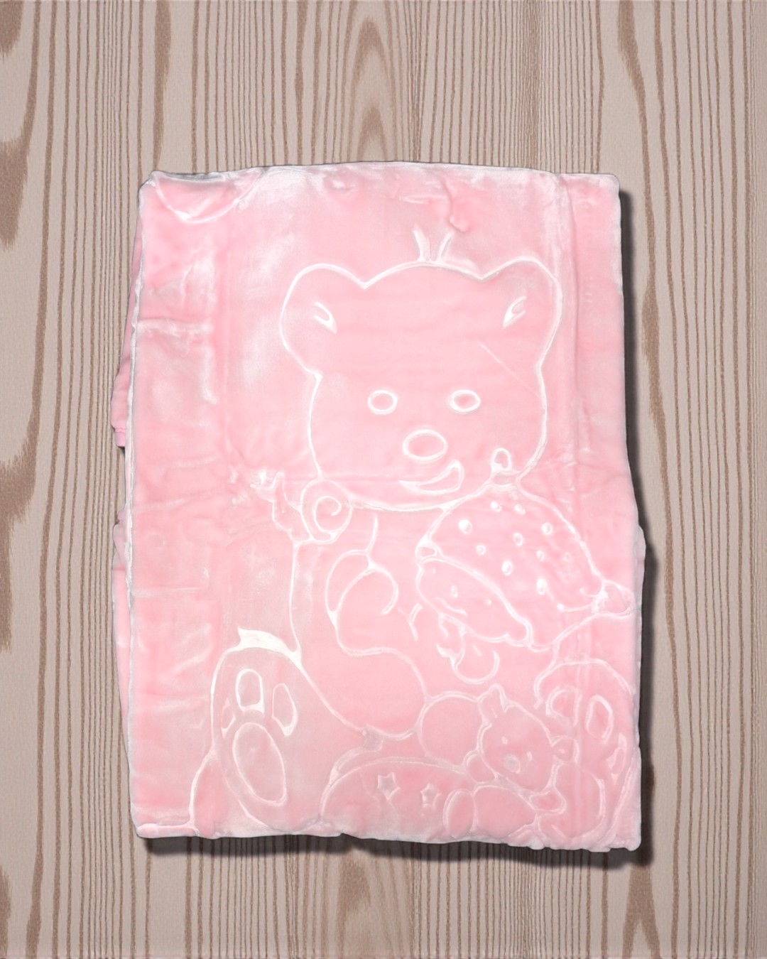 Cobertor rosa aveludado com padrão de ursinho em relevo sobre mesa de madeira clara