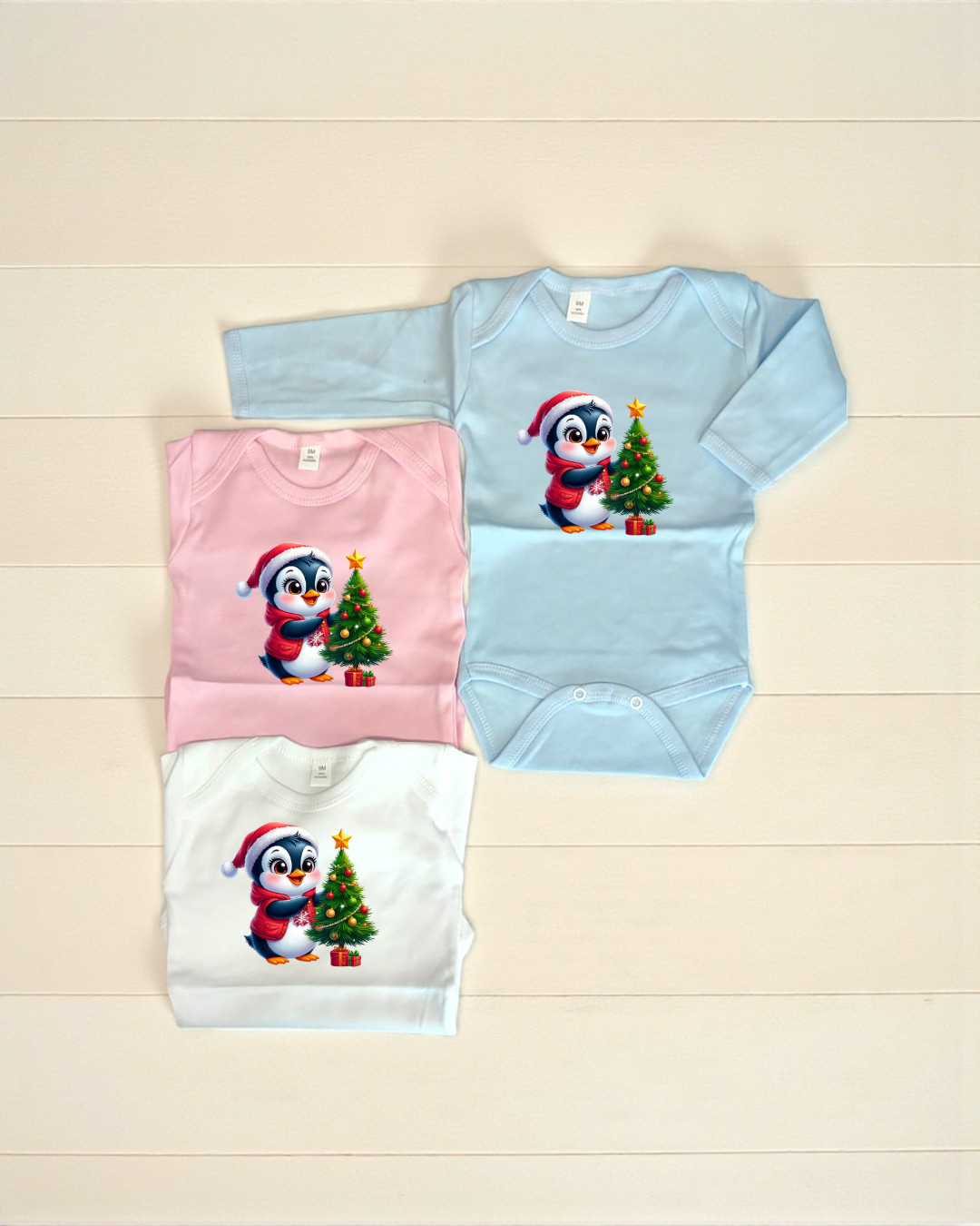 Bodies infantis azul claro, rosa e branco com estampa natalícia de pinguim decorando árvore de Natal.