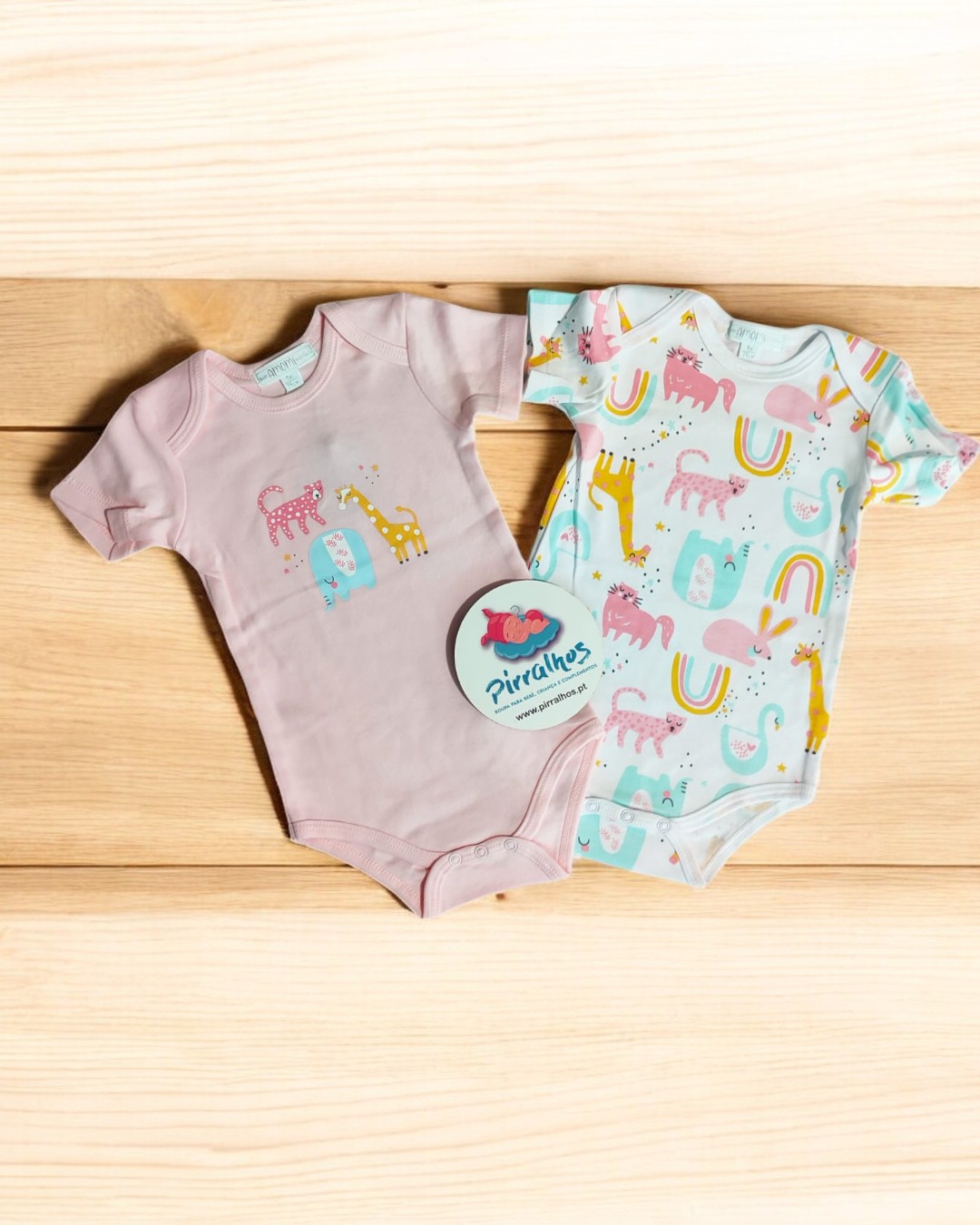 Dois bodies de bebé com estampados coloridos sobre superfície de madeira clara
