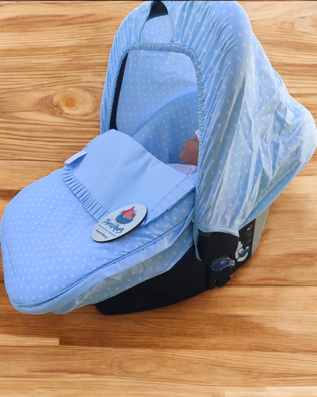 Cadeira para bebé azul com padrão de corações brancos, etiqueta redonda e piso de madeira.