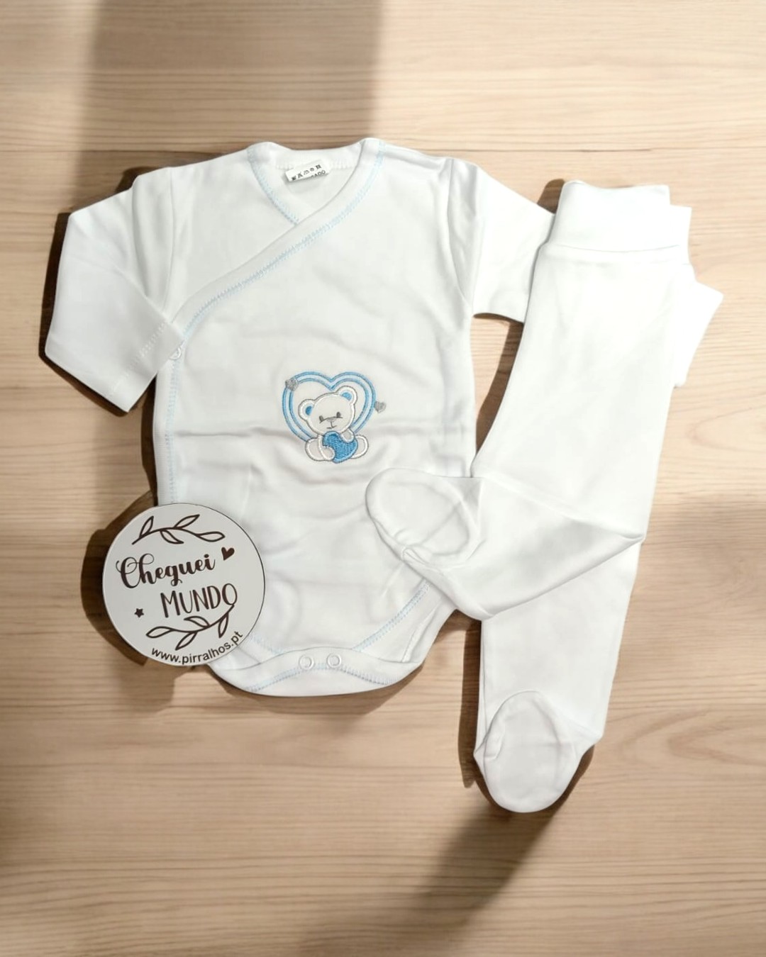 Conjunto de roupa de bebé branco com ursinho azul e círculo decorativo com texto
