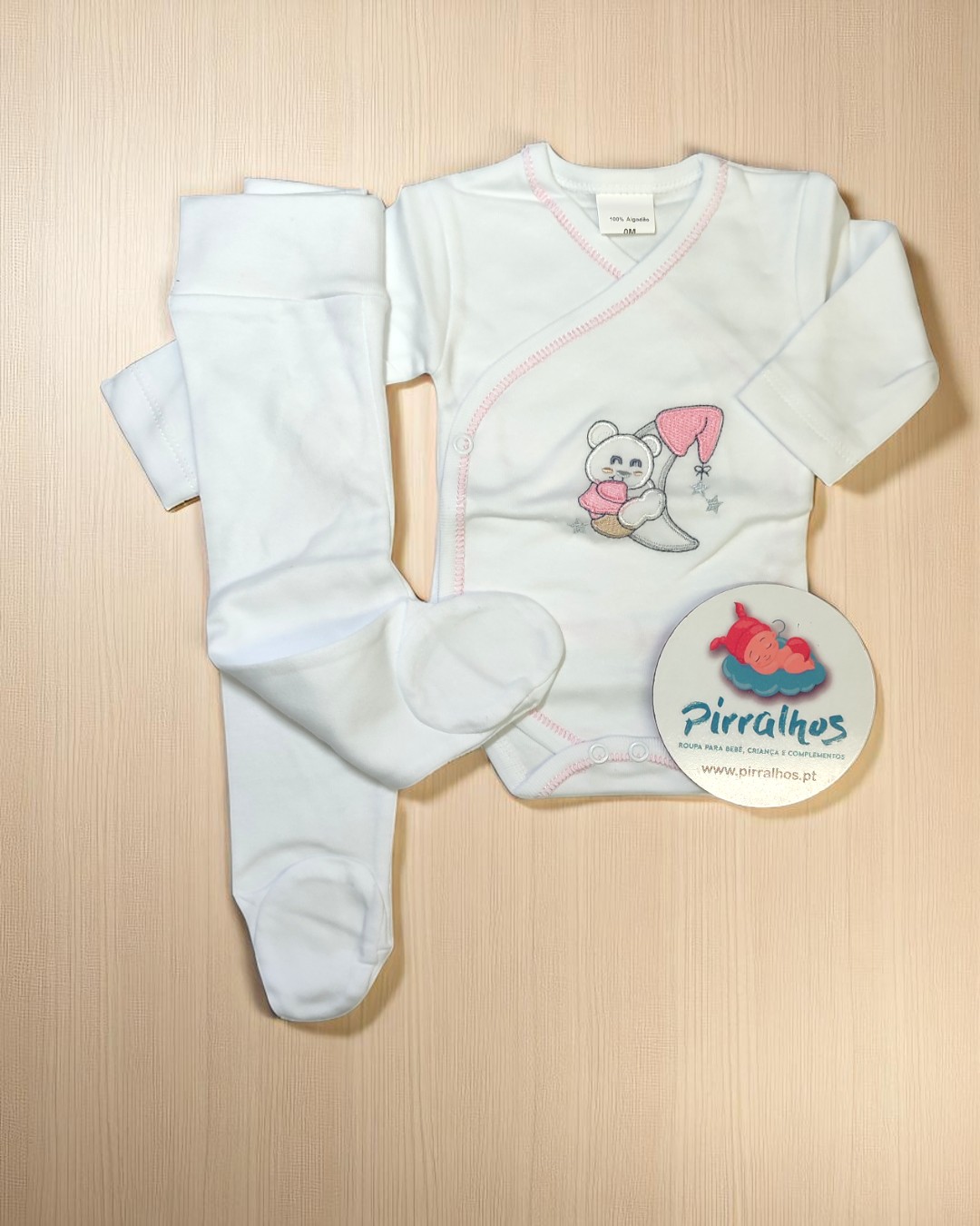 Conjunto de bebé branco com body bordado e meia-calça sobre fundo de madeira clara